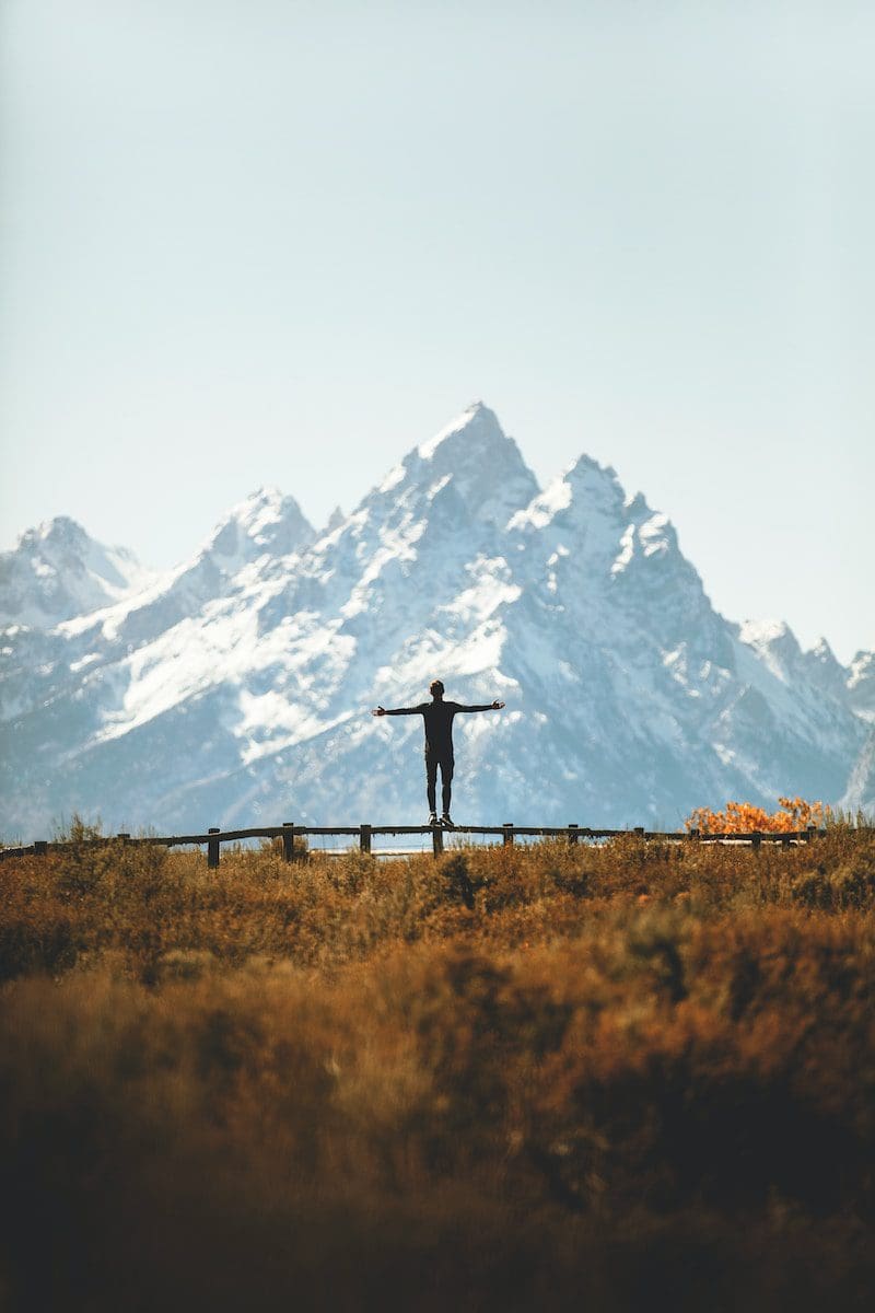 man standing on fence overlooking mountain in backcountry
