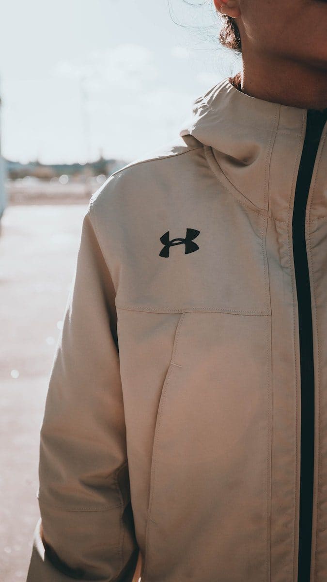 woman standing while wearing white Under Armour zip-up jacket for cash back
